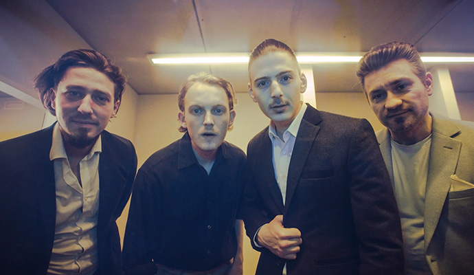 Vier Personen in Anzug und Hemd schauen fasziniert auf eine gelb getönte Scheibe.