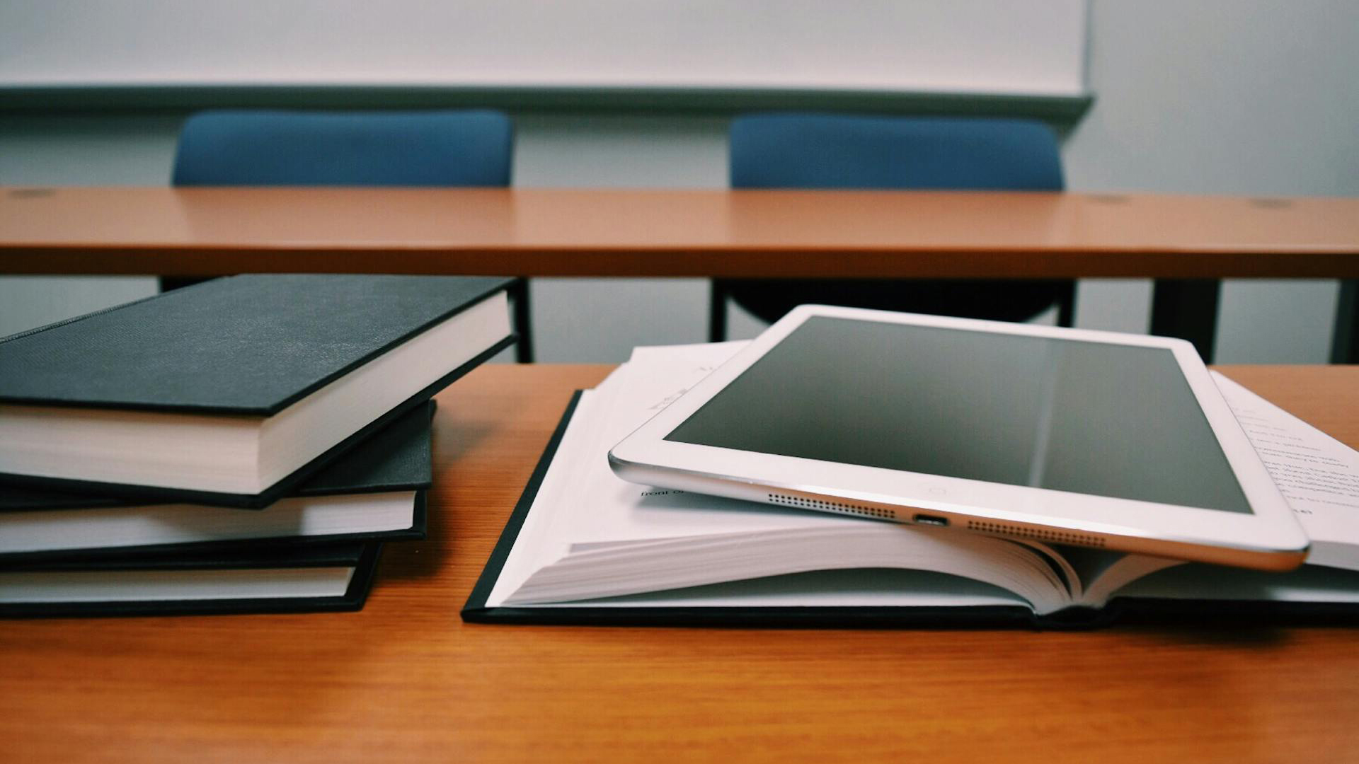 Ein Klassenraum mit zwei Tischen voreinander auf dem vordersten liegen ein Stapel Bücher und ein Tablet auf einem Buch.