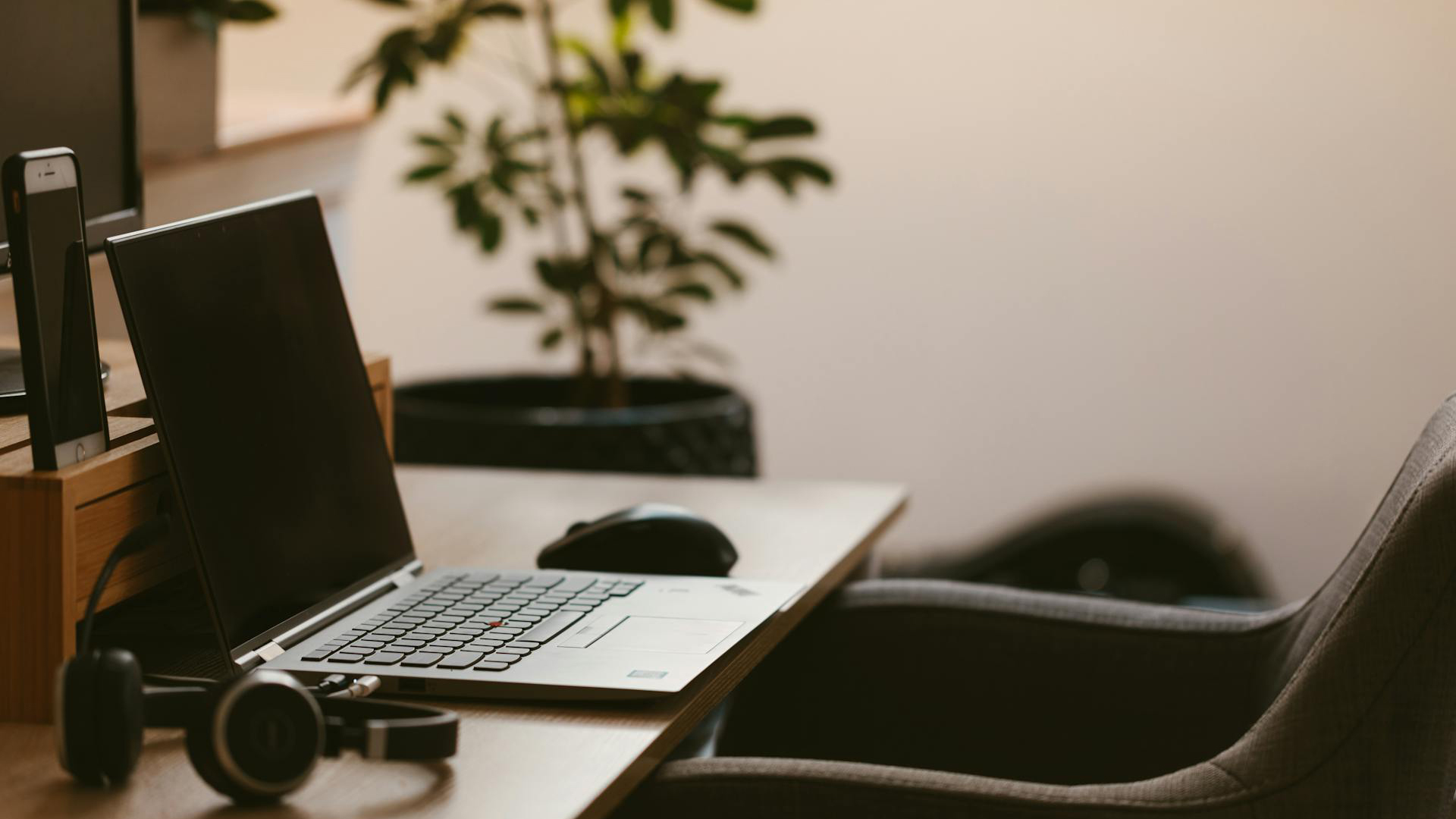 Ein Schreibtisch, auf dem ein Laptop, Kopfhörer und eine Maus liegen, mit angerücktem Stuhl.