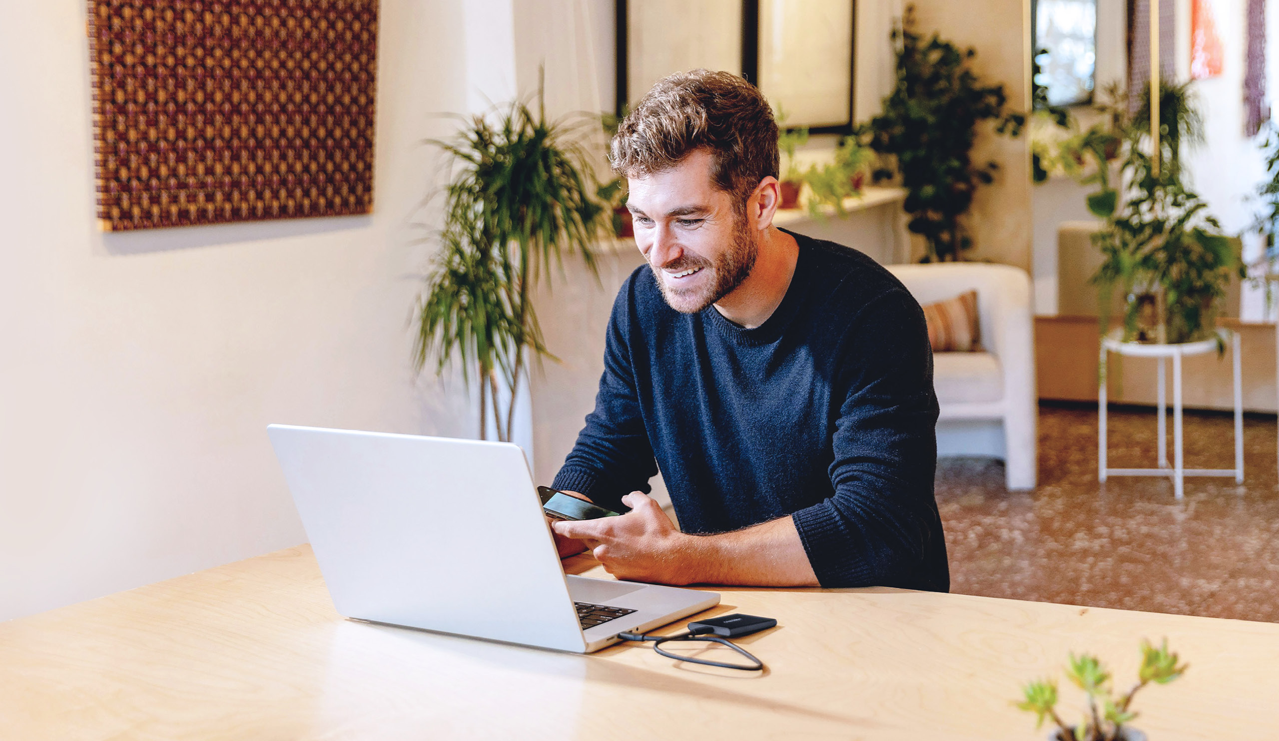 Ein Mann, der lächelnd vor einem Laptop sitzt.