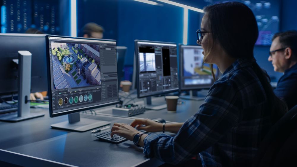 Eine Frau die vor einem Monitor sitzt und arbeitet. Auf dem Monitor ist ein 3D-Grafikprogramm zu sehen.