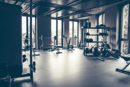 Ein Fitnessstudio mit mehreren Geräten wie Seilzug, Rudermaschine, Boxsack, Hanteln und vieles mehr.