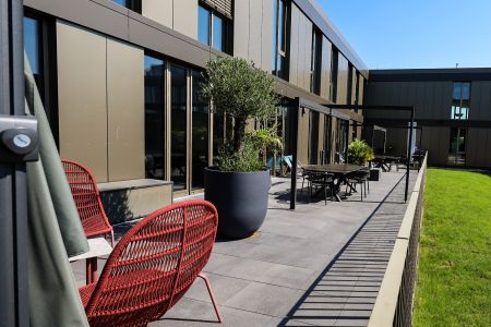 Sonnentrasse mit Grünpflanzen, Sonnenschirmen und mehreren Sitzmöglichkeiten.