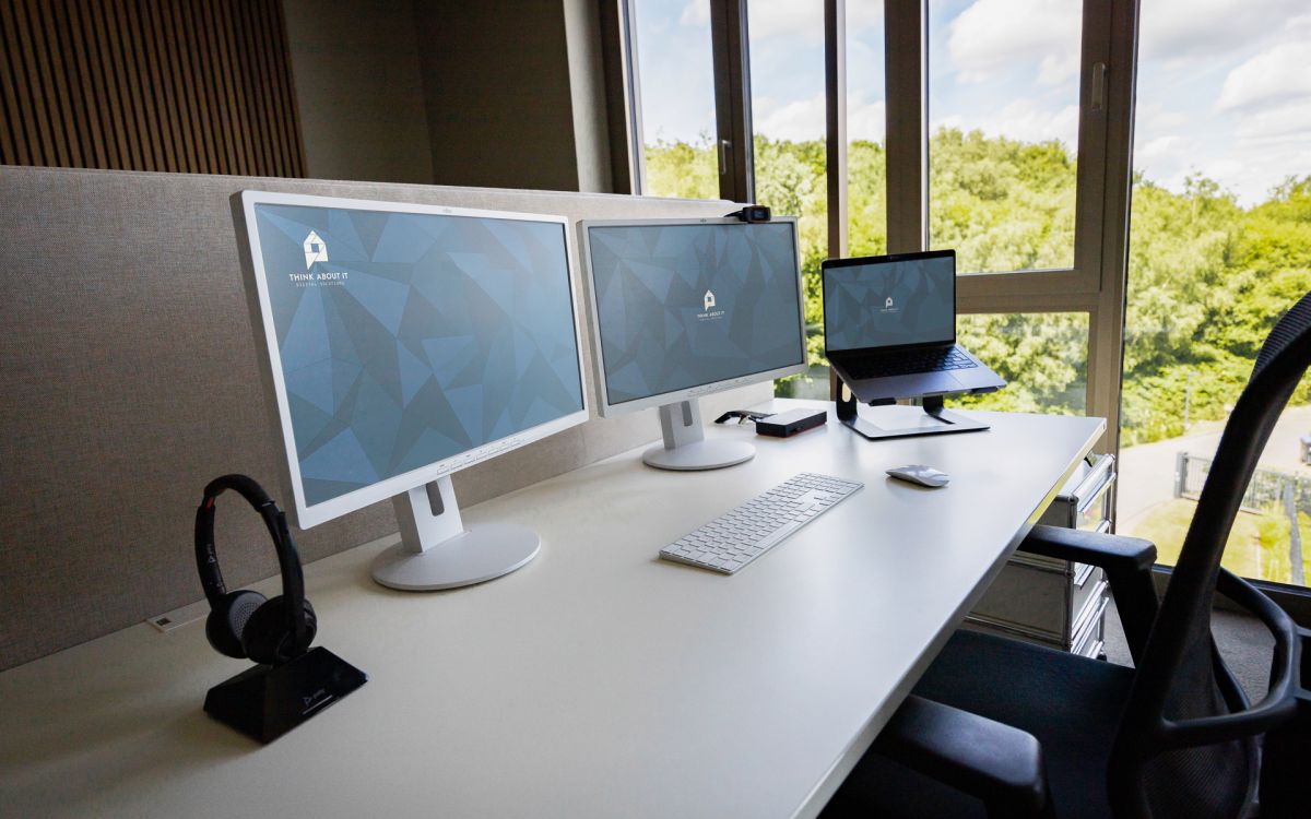 Ein Arbeitsplatz, ausgestattet mit einem Headset, zwei Monitoren, einer Videokamera, einem MacBook und einem Bürostuhl.