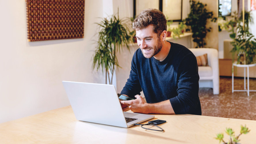 Ein Mann, der lächelnd vor einem Laptop sitzt.